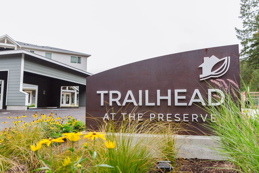 a sign for trailhead at the preserve with flowers in front of it