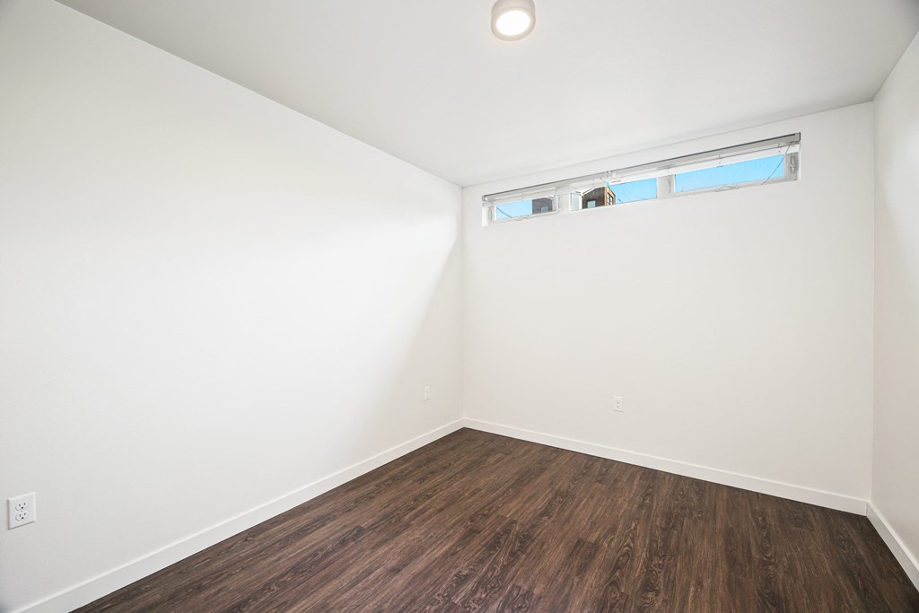 a bedroom with white walls and wood flooring and a window