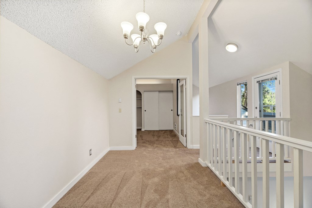 the landing of a home with a staircase and a door to a hallway with carpet