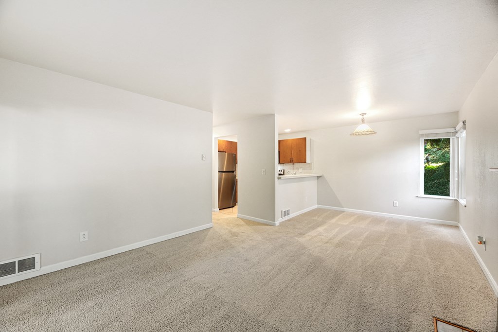 the living room and kitchen of an empty house with carpeting and a window