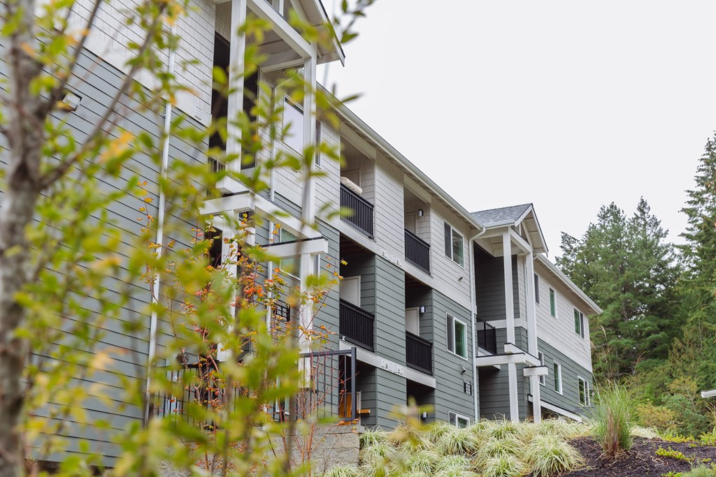 an apartment building with gray siding and green trees