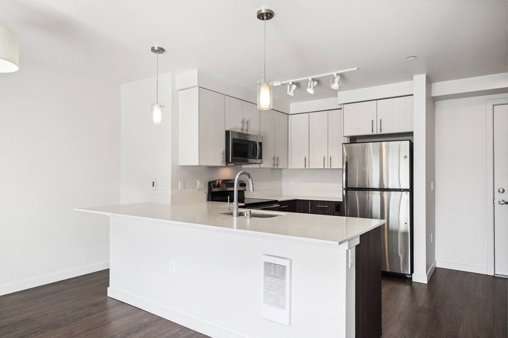 a white kitchen with a large island and stainless steel refrigerator