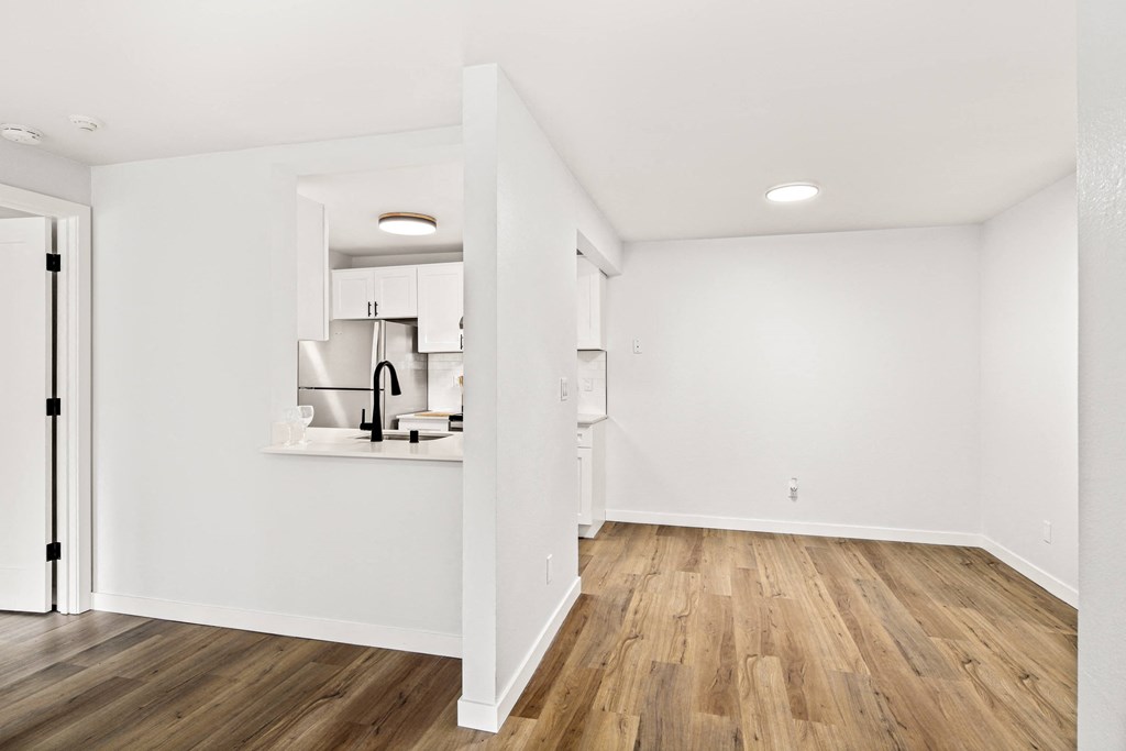 a living room and kitchen with white walls and wood floors