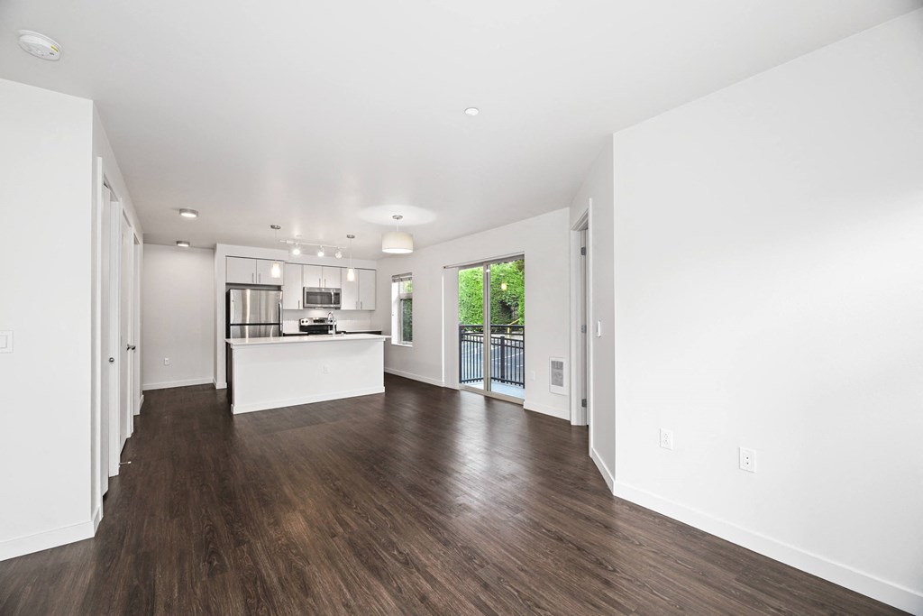a living room and kitchen with white walls and wood floors