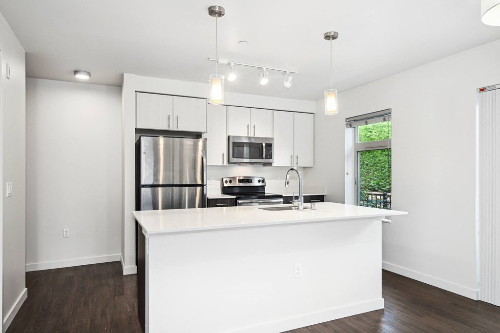 a white kitchen with a large island and a stainless steel refrigerator