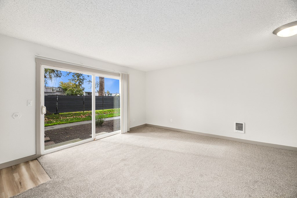an empty living room with a sliding glass door to a yard