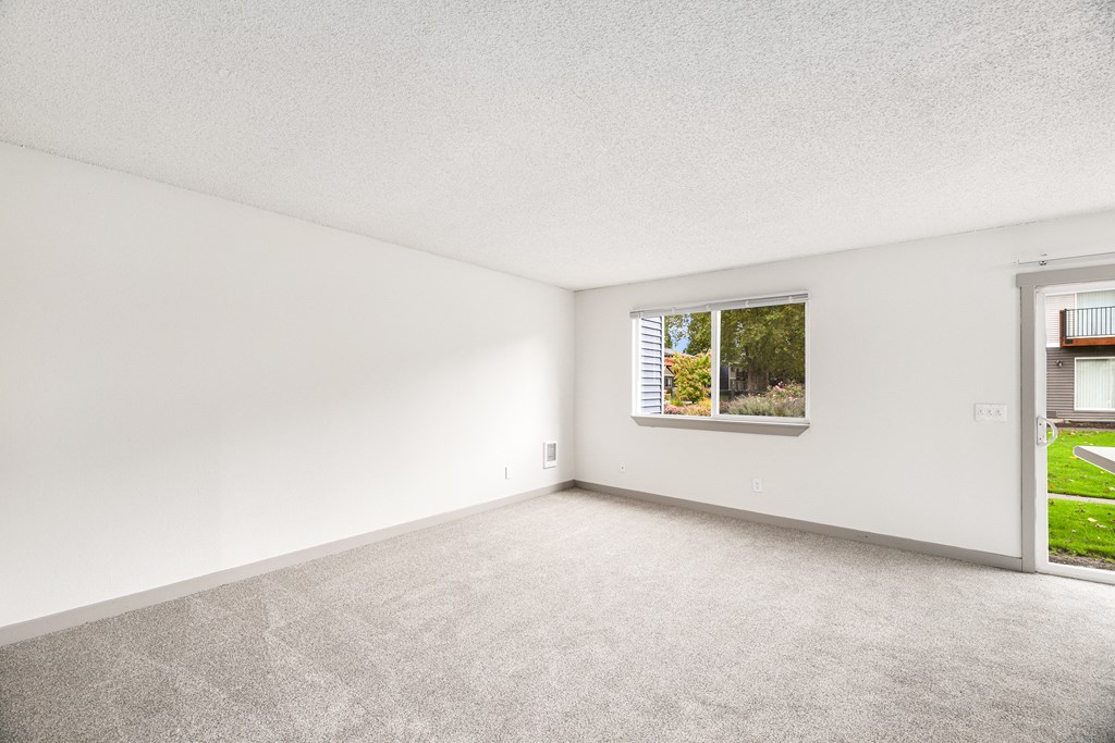 the living room of an apartment with carpet and a window