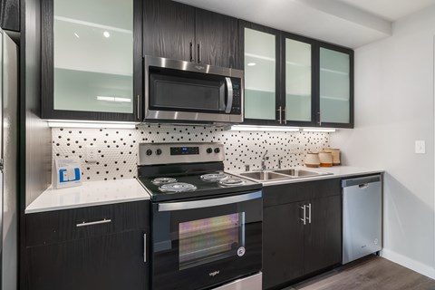 A modern kitchen with black cabinets and a stainless steel refrigerator.