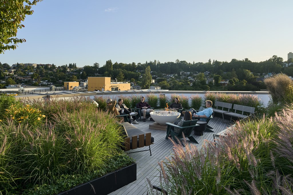 A group of people are sitting around a fire pit on a wooden deck.