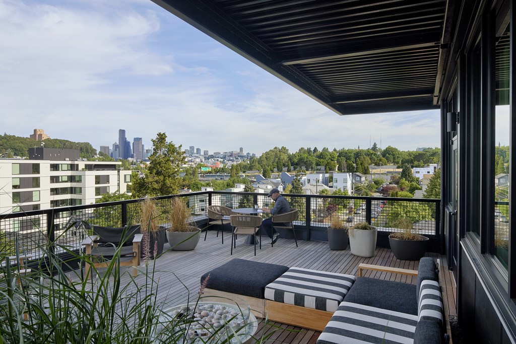 A man is sitting on a chair on a balcony with a view of the city.