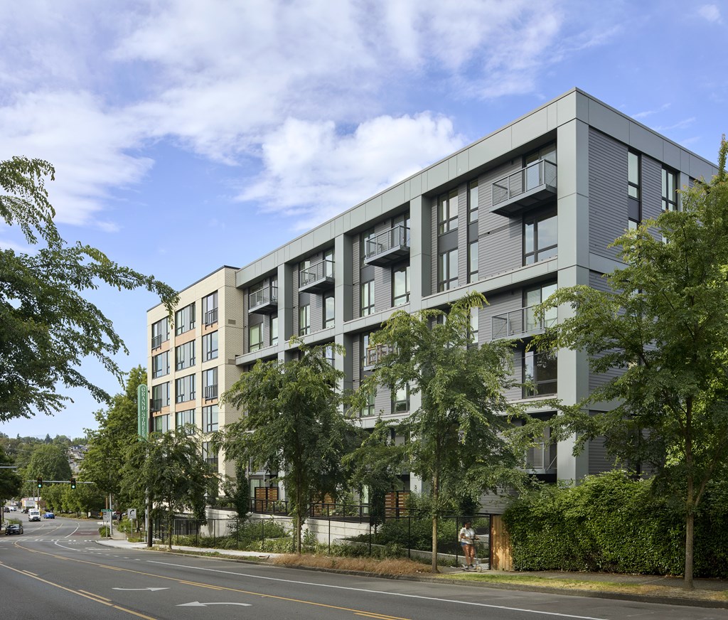 A modern apartment building with balconies and trees in front.
