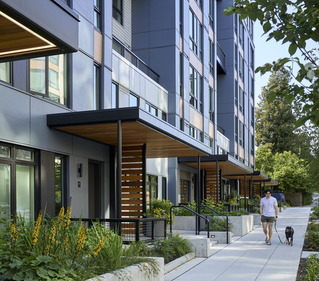 A man walking his dog on a sidewalk in front of a modern building.