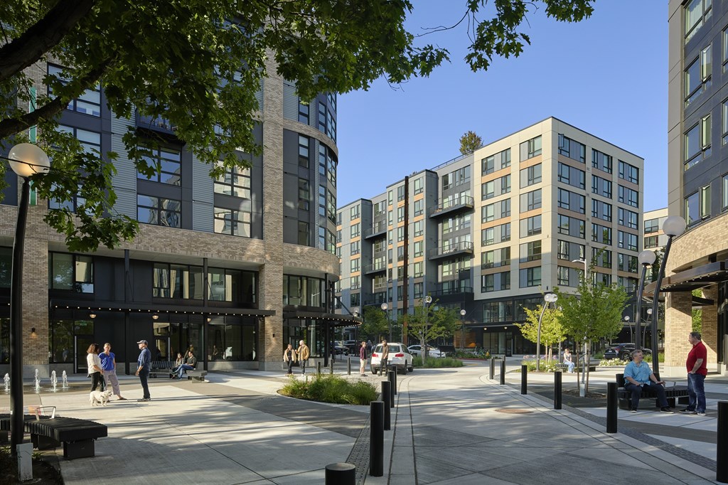 A city street with people walking and sitting on benches.