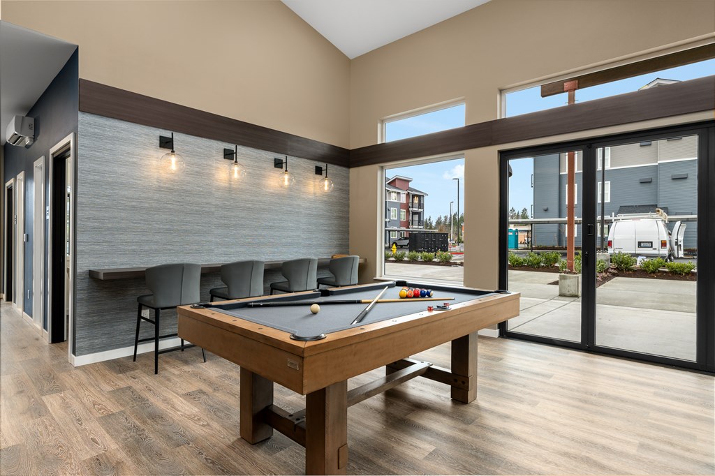 A pool table is in the middle of a room with a wood floor and a wall with lights.