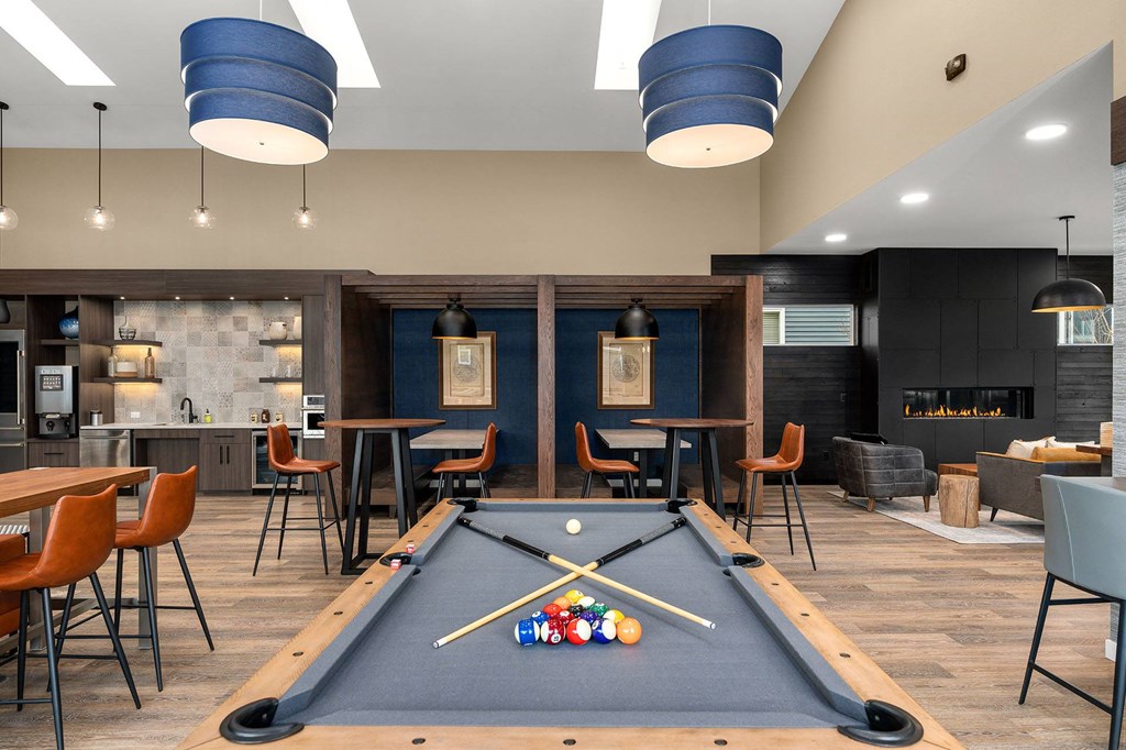 A pool table is in the middle of a room with a bar and chairs.