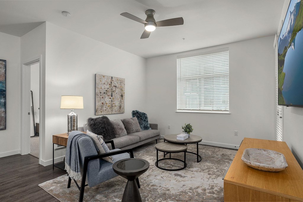 A living room with a grey couch, a small table, and a fan.