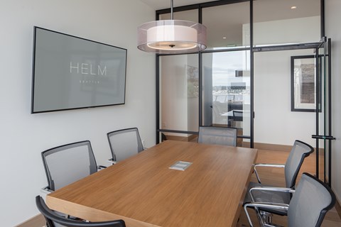 A conference room with a long table and chairs, a framed picture on the wall, and a glass partition to the right.