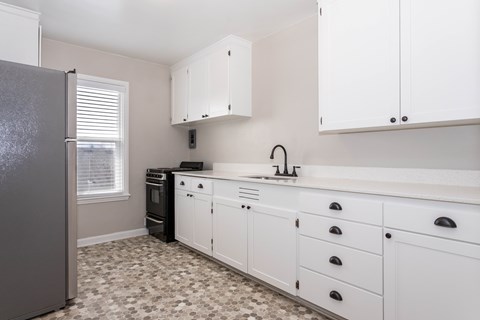 A kitchen with white cabinets and a black fridge.