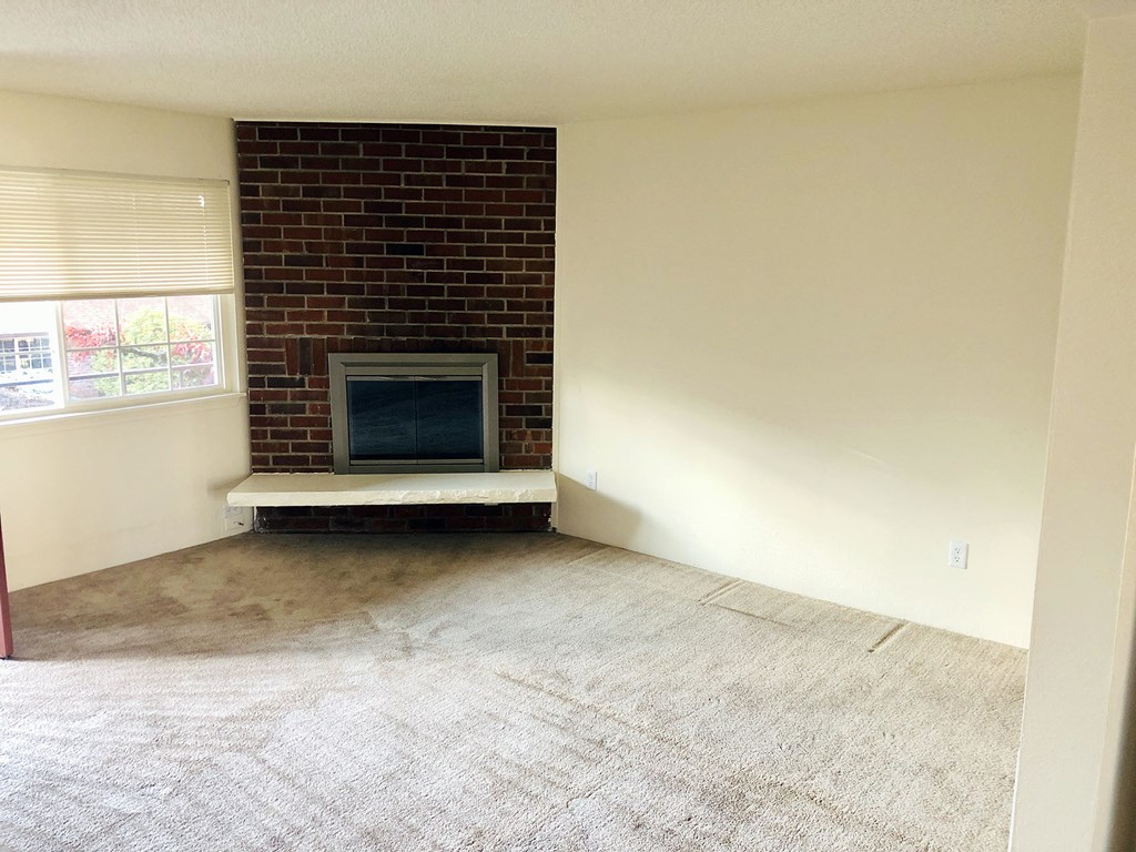 an empty living room with a brick fireplace and a wooden floor