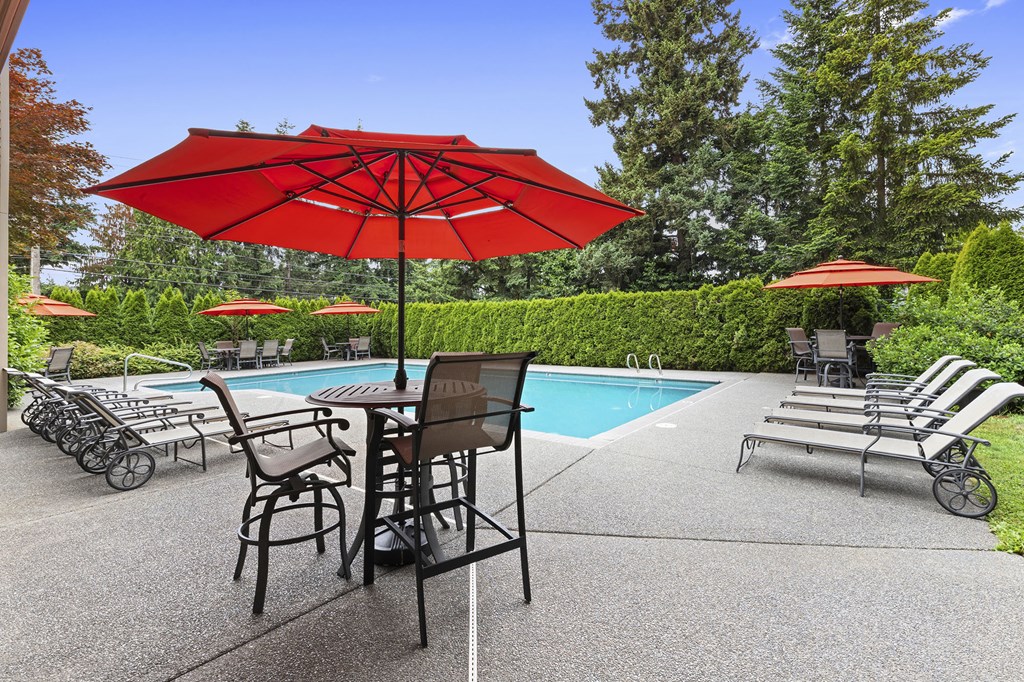 a swimming pool with a red umbrella and tables with chairs
