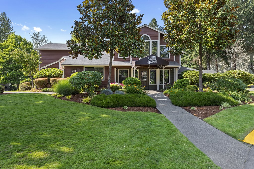 a house with a sidewalk in front of a lawn and trees