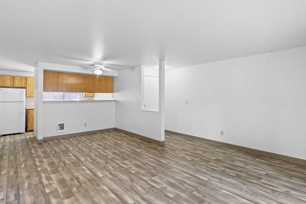 an empty living room with wood flooring and a kitchen