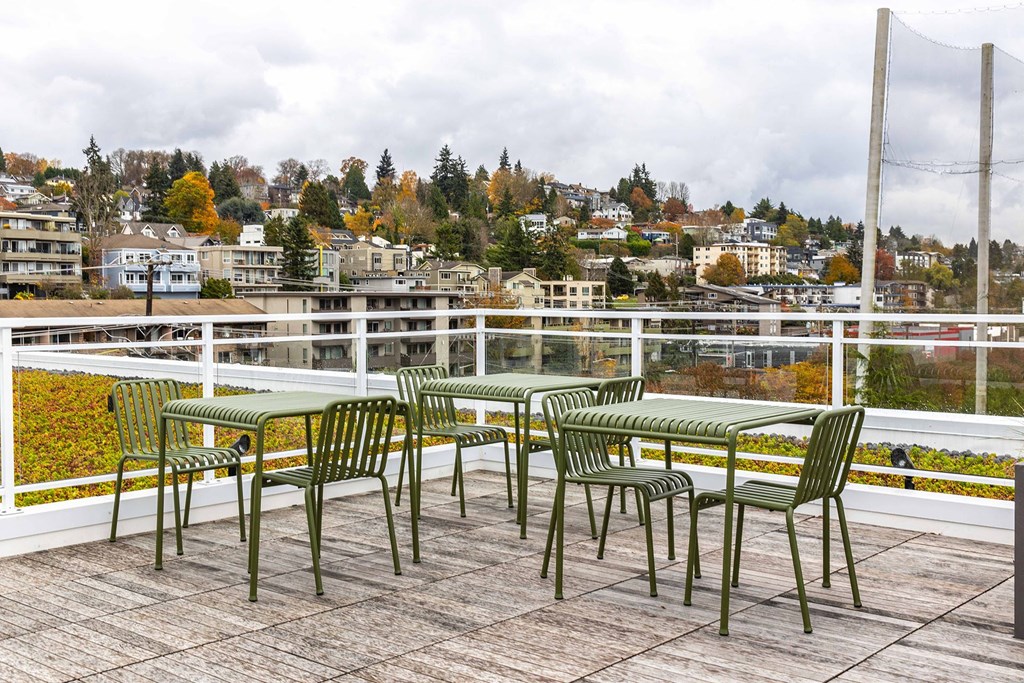 a patio with green chairs and tables on a balcony overlooking a city