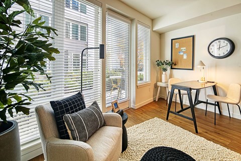 A living room with a beige couch, a black hat, a white table, and a clock on the wall.