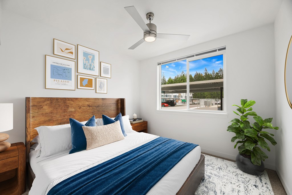 A bedroom with a bed, a ceiling fan, and a window with a view of a parking lot.