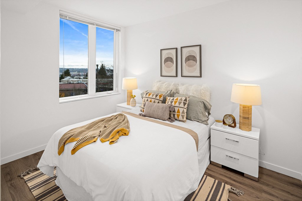 a bedroom with a large window and a bed with white sheets and pillows