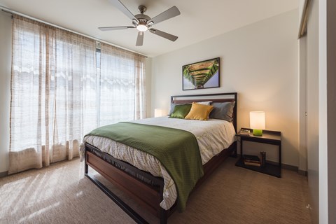 A bedroom with a bed, a ceiling fan, and a painting on the wall.