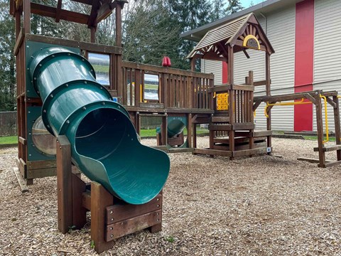 A playground with a green slide and wooden structures.