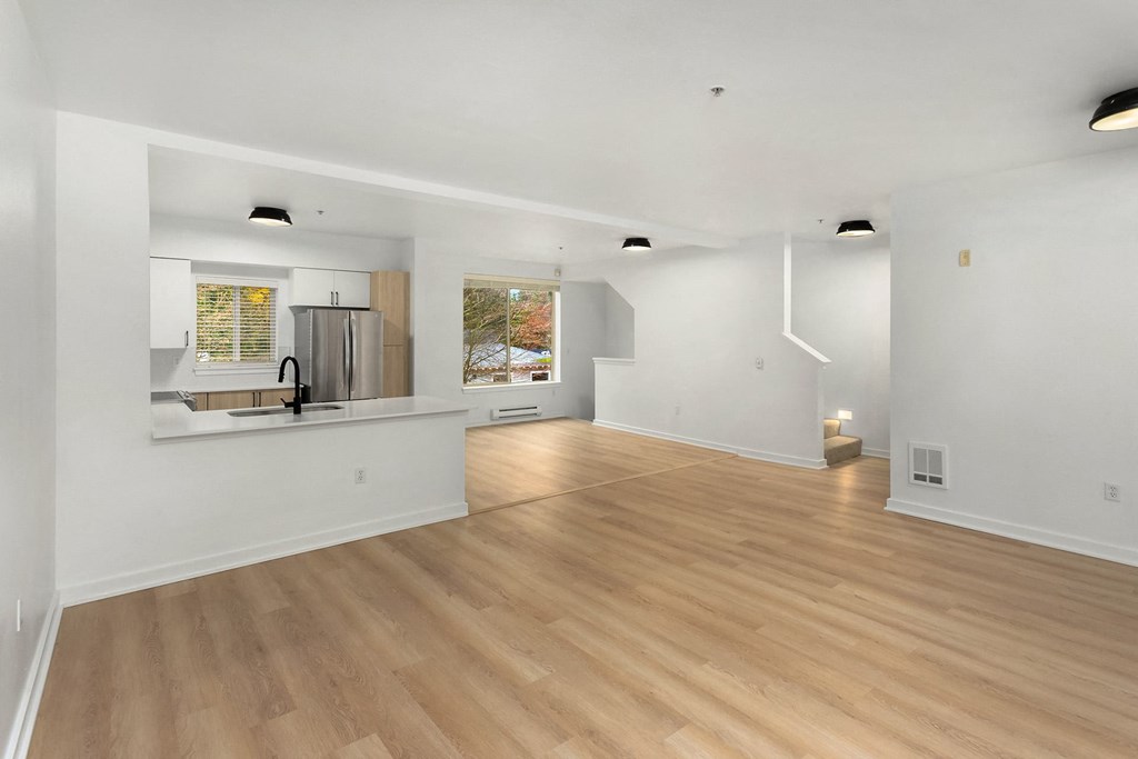 the living room and kitchen of a house with white walls and wood floors