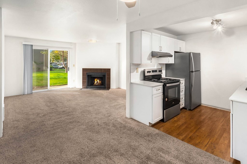 an empty living room with a kitchen and a fireplace