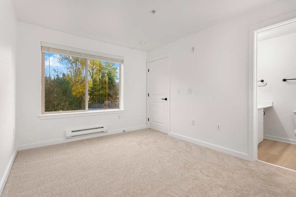 a bedroom with a large window and white walls and carpet