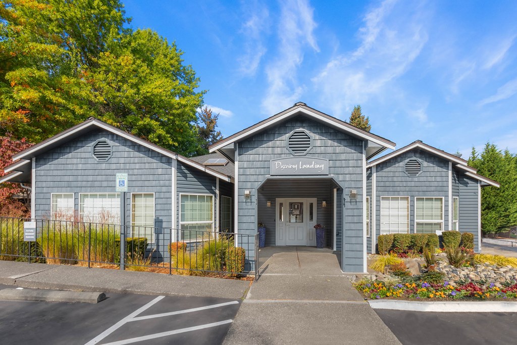 the front of a grey building with a driveway and a gate