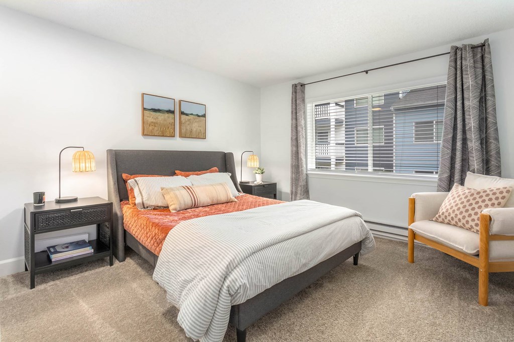 A bedroom with a bed, chair, and nightstand.