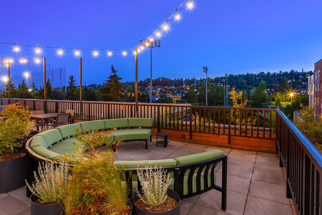 a roof deck with furniture and a city at night