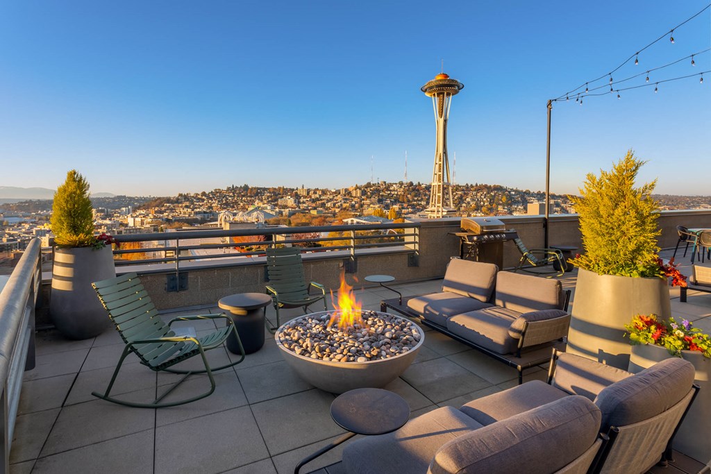 a rooftop patio with a fire pit and chairs and a view of the space needle