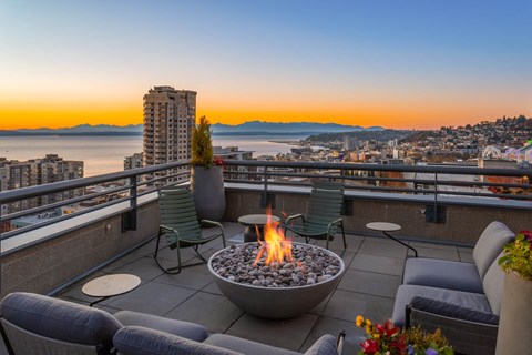 a patio with a fire pit overlooking the ocean and the city at sunset