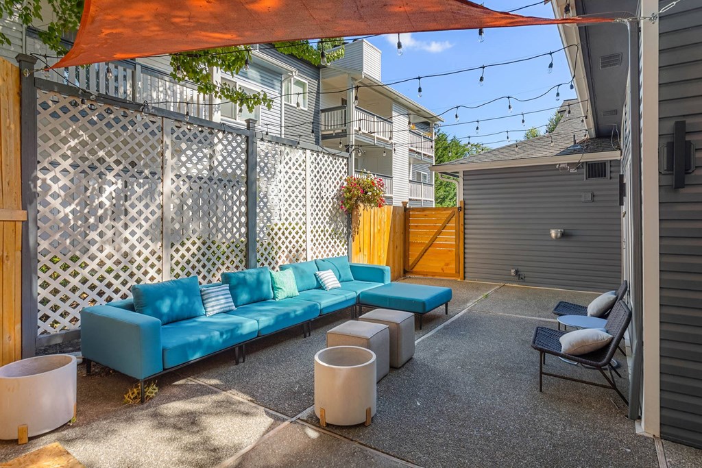 A blue couch is in the middle of a patio with a white table and a black chair.