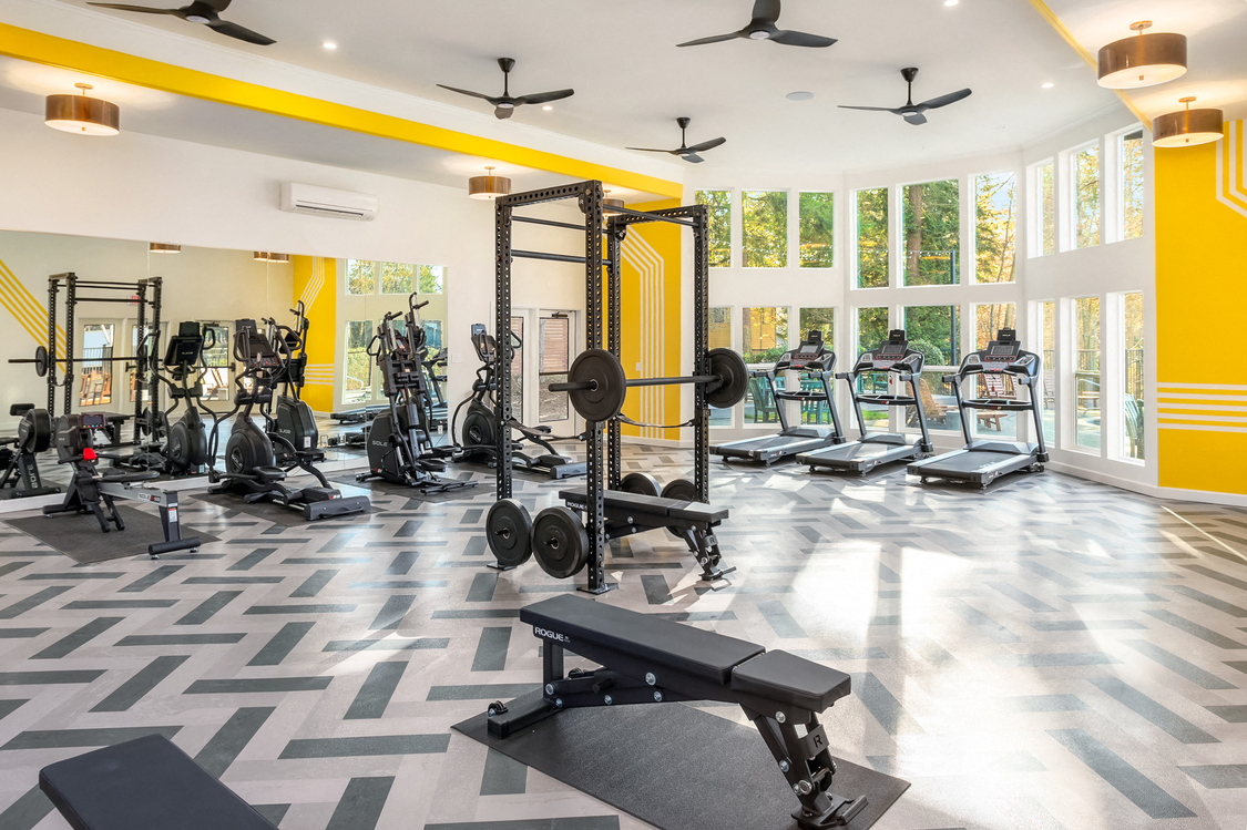 a gym with weights and cardio equipment in a large room with windows