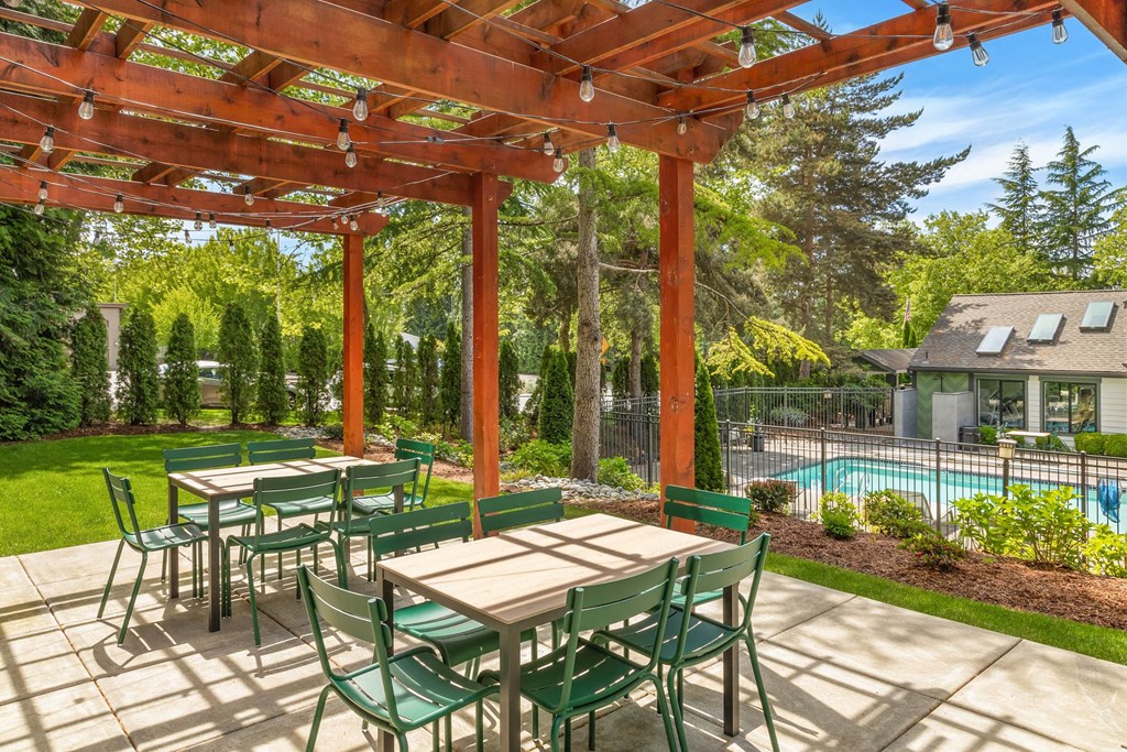 a patio with wooden tables and chairs and a pool in the background