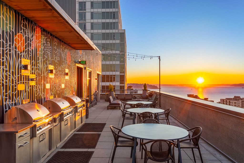 a terrace with tables and chairs overlooking the ocean at sunset
