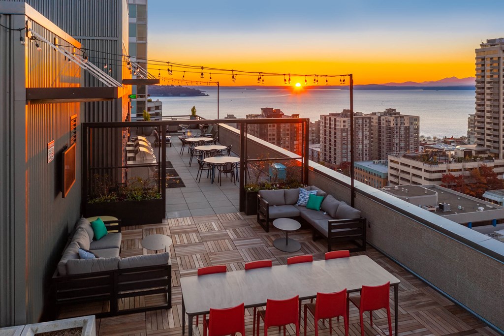 a rooftop terrace with a view of the city and the ocean at sunset
