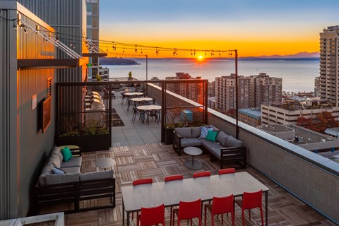a rooftop terrace with a view of the city and the ocean at sunset