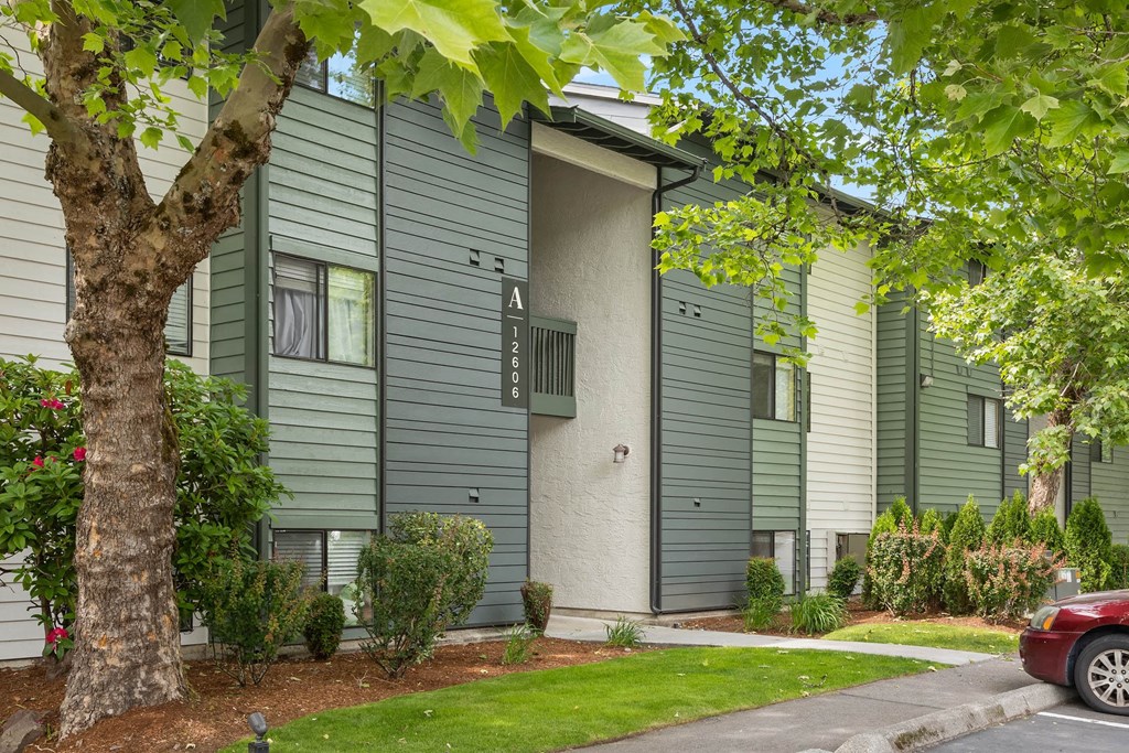 a gray and green apartment building with a red car parked in front of it