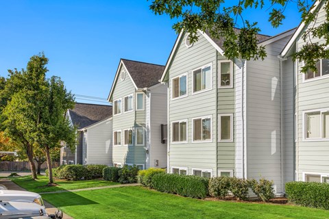 a row of white houses with a green lawn and trees