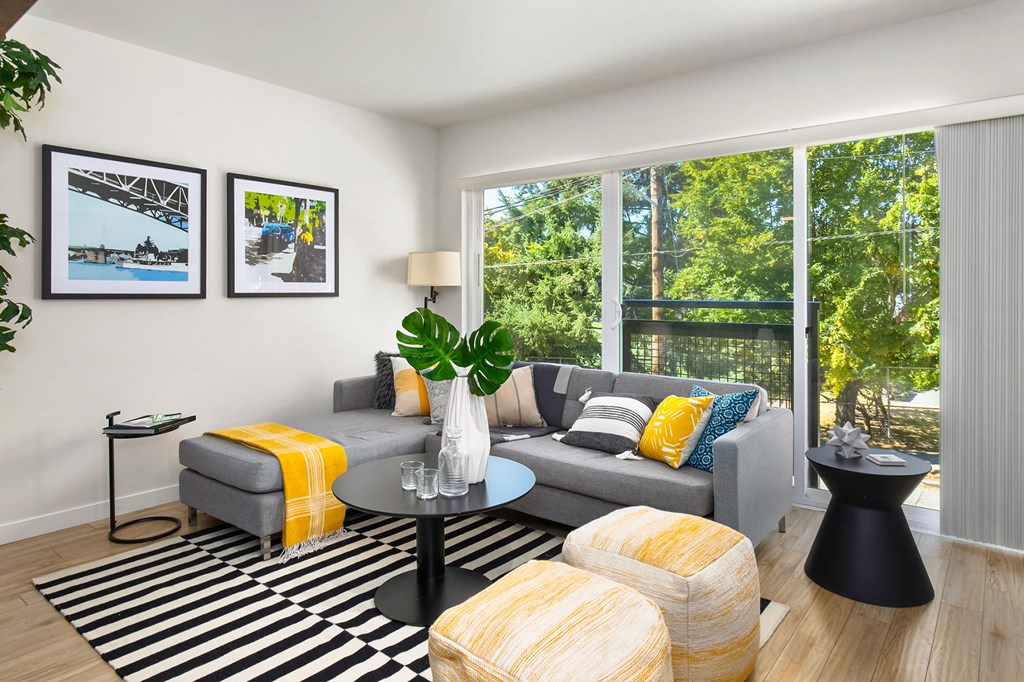 a living room with a gray couch and yellow pillows and a large window
