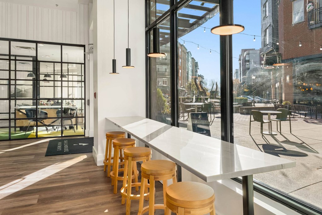 a long white table with wooden stools in front of a large window